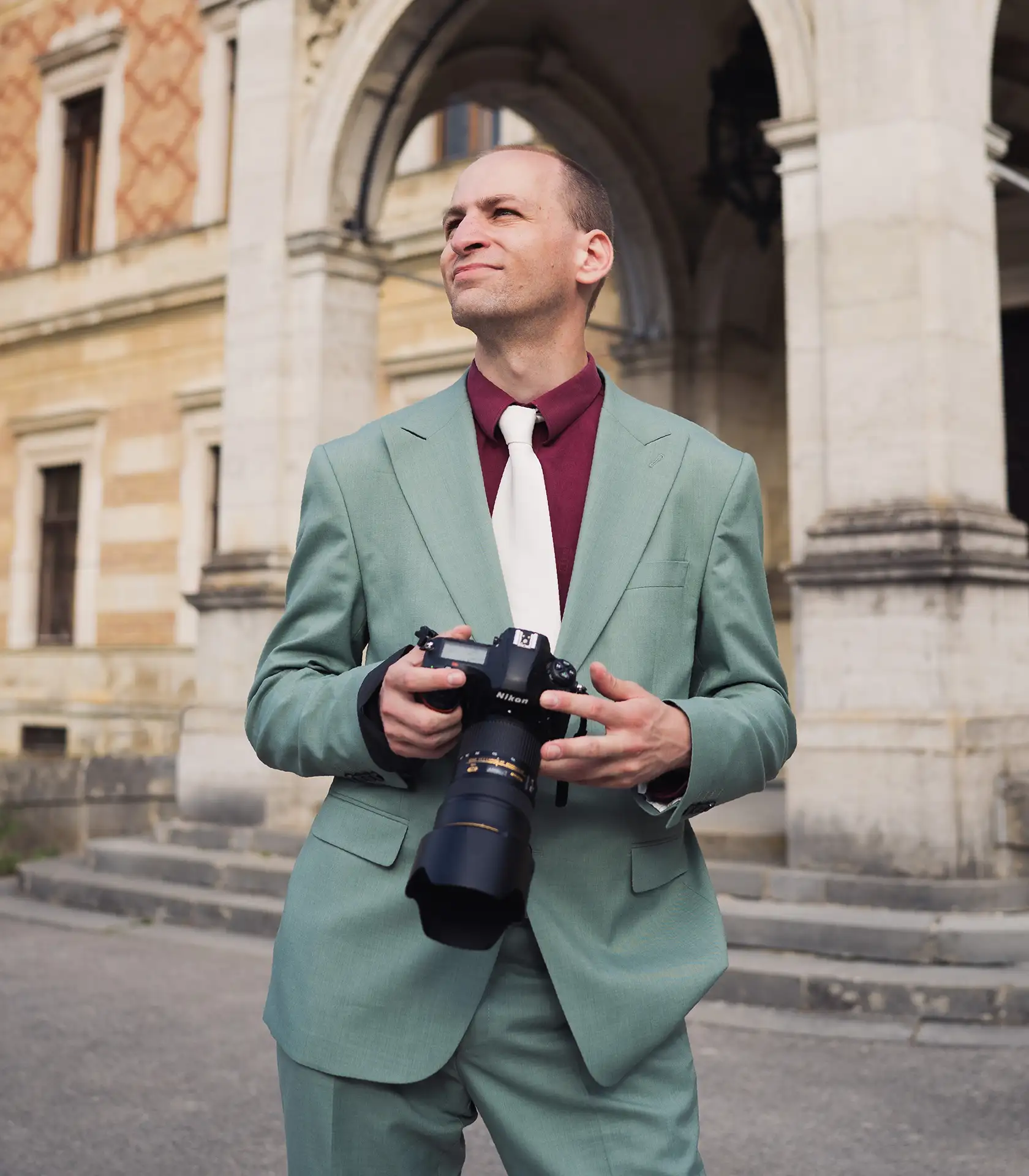 Wedding photographer standing confidently with a camera at an Austrian palace in a green suite at a wedding
